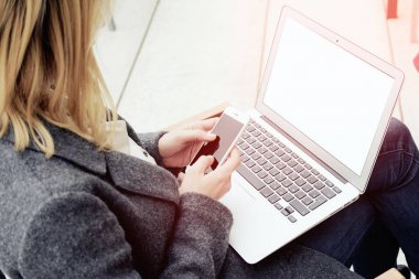 Genç kadının dizlerinin üstünde laptop ile otururken smartphone kullanarak resim kırpılmış