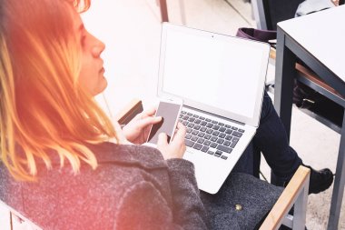 Genç kadının dizlerinin üstünde laptop ile otururken smartphone kullanarak resim kırpılmış