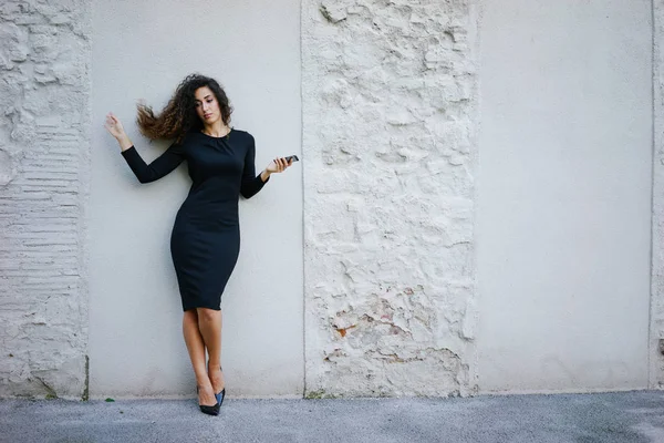 Młoda Kobieta Piękne Długie Kręcone Włosy Czarnej Sukience Jej Smartfona — Zdjęcie stockowe