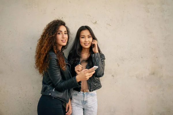 Twee Mooie Jonge Vrouwen Met Smartphones Poseren Tegen Betonnen Muur — Stockfoto