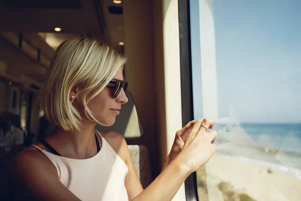 若い女性が移動列車からスマート フォンと海の風景を撮影 — ストック写真