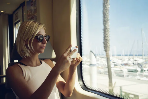 young woman shooting landscape with smartphone from moving train