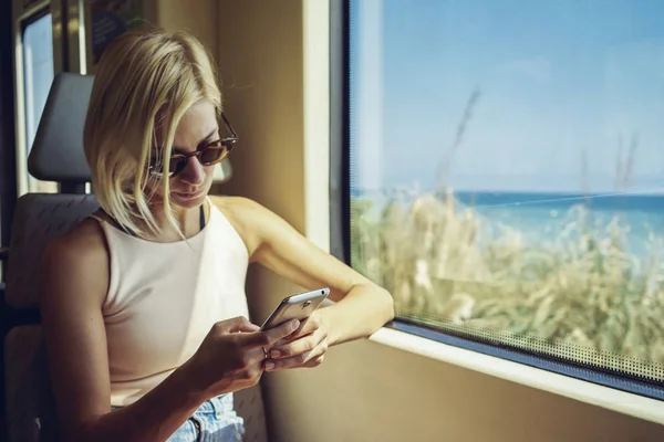 若い女性が窓の近く 動いている電車でスマート フォンを使用して — ストック写真