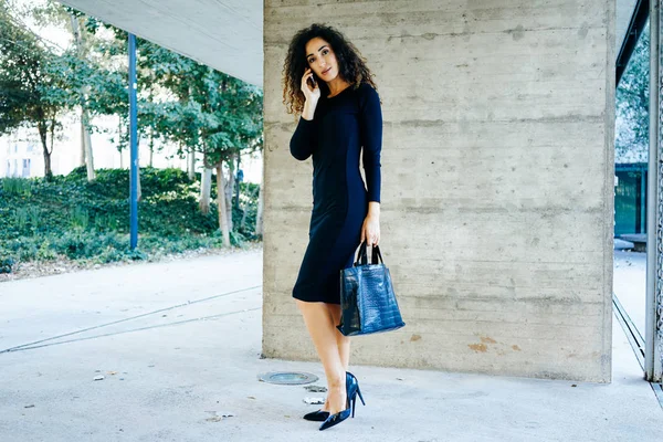 スマート フォン屋外で話黒のドレスで美しい若い実業家 ストック写真