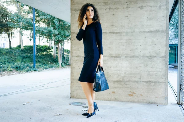 スマート フォン屋外で話黒のドレスで美しい若い実業家 ストック画像