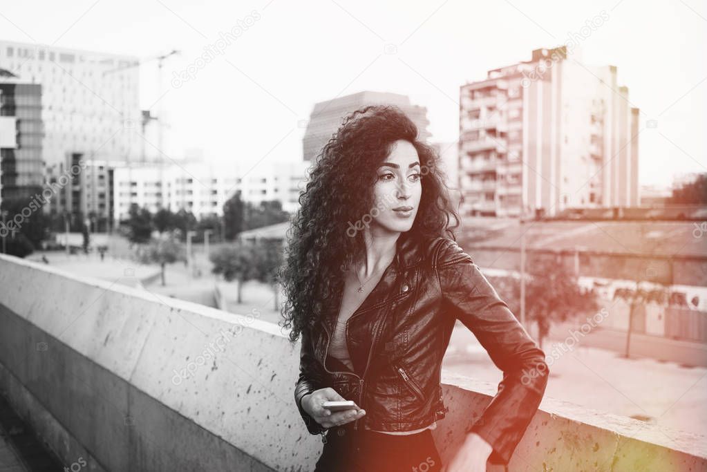 Portrait of beautiful brunette young woman using smartphone on a city buildings background