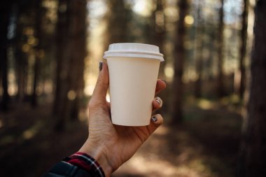 Orman arka plan üzerinde plastik kapaklı bir boş kağıt bardak tutan el