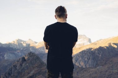 dağ arka plan üzerinde siyah bir boş t-shirt giyen genç hipster adam. Arkadan görünüm
