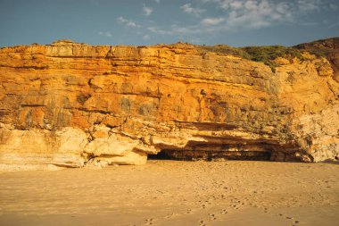 Gün batımı sırasında kum plajındaki kayalık dağ
