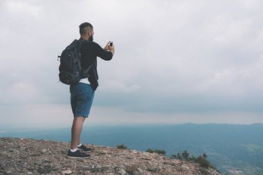Young male tourist taking pictures with smartphone of beautiful landscape clipart
