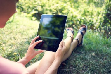 Genç kadın şehir parkı çim üzerinde otururken tablet kullanma