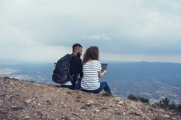 Young tourists with backpacks enjoying and shooting valley view on a digital tablet  from top of a mountain