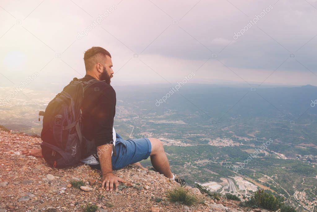 Man sitting on the peak of rock and watching into colorful mist and fog in forest valley.