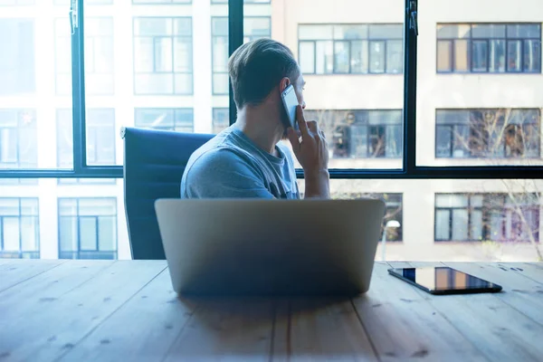 Junger Geschäftsmann Arbeitet Laptop Während Büro Mit Dem Smartphone Spricht — Stockfoto