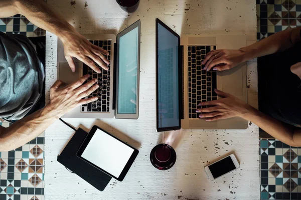 Cropped image of male and female hands typing on the keyboard opposite of each other. various gadgets on the desktop