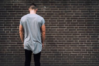 bir tuğla üzerinde bekleyen bir boş gri t-shirt giyen yakışıklı delikanlı duvar arka plan 