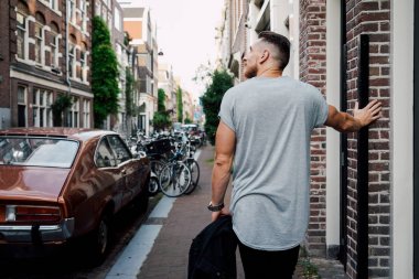 boş bir gri t-shirt giyen yakışıklı kaslı adam açık havada tuğla duvarın duruyor