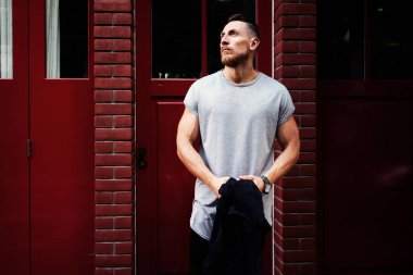 Çekici genç kaslı adam kırmızı duvar bir arka plan üzerinde bekleyen bir gri T-shirt giyiyor 