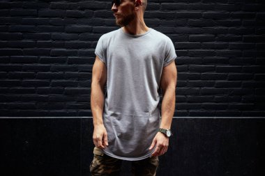sakallı bir kaslı erkek modeli siyah tuğla duvar arka plan üzerinde duran boş bir gri t-shirt giyen kırpılmış görüntü