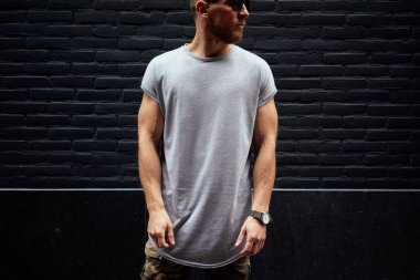 sakallı bir kaslı erkek modeli siyah tuğla duvar arka plan üzerinde duran boş bir gri t-shirt giyen kırpılmış görüntü