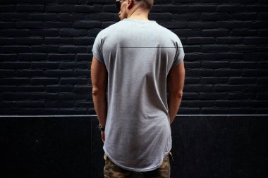 sakallı bir kaslı erkek modeli siyah tuğla duvar arka plan üzerinde duran boş bir gri t-shirt giyen kırpılmış görüntü