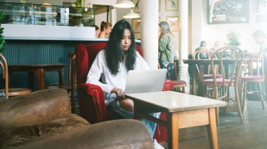 Casual Asyalı genç kadın kahve dükkanında mesafe iş için dizüstü bilgisayar kullanarak