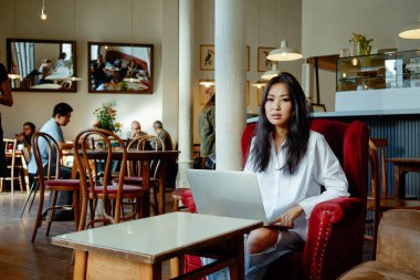 Casual Asyalı genç kadın kahve dükkanında mesafe iş için dizüstü bilgisayar kullanarak