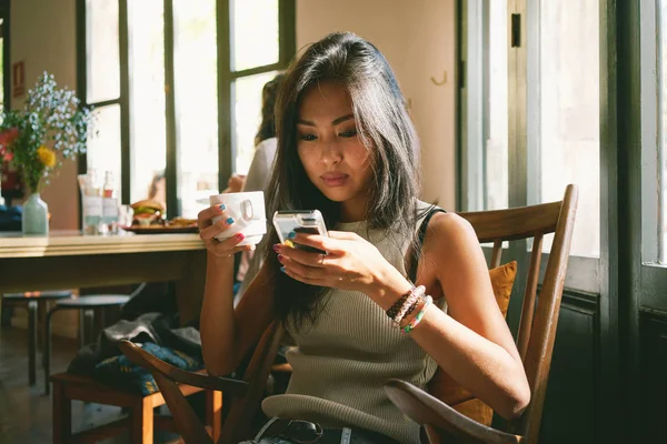 Ung Vakker Asiatisk Kvinne Som Bruker Smarttelefon Mens Hun Drikker – stockfoto