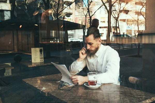 young employee analyzing financial data while sitting next to big window in coffee shop