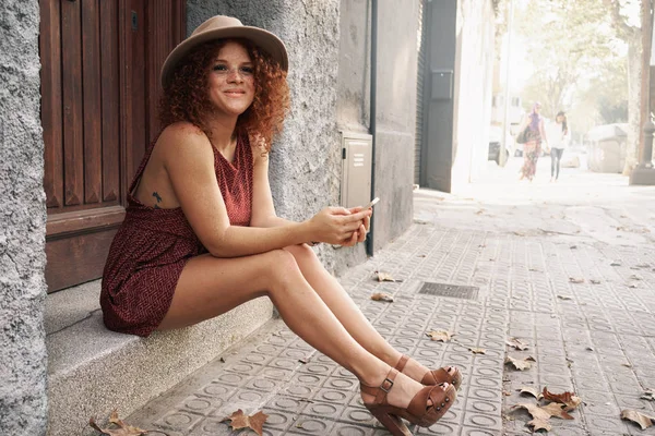 Atrakcyjna Młoda Kobieta Czerwone Włosy Kręcone Siedząc Schodach Smartphone Przy — Zdjęcie stockowe