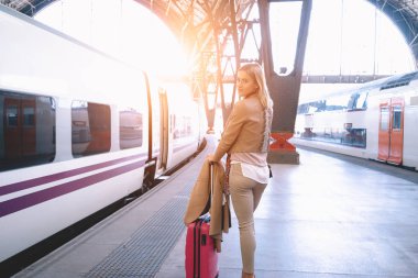 tren tren istasyonunda bekleyen genç güzel modern iş kadını. Genç ve güzel giyimli kadın bir bavulla tren platformu üzerinde gider.