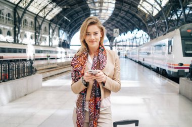 genç çekici işkadını tren istasyonu platformu üzerinde Treni beklerken Smartphone kullanarak