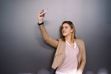 sarı saçlı genç çekici işkadını selfie gri bir arka plan üzerinde yapar. 