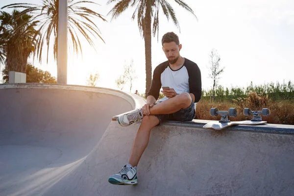 Pemuda Tampan Menggunakan Smartphone Saat Sedang Istirahat Taman Bermain Skateboard — Stok Foto