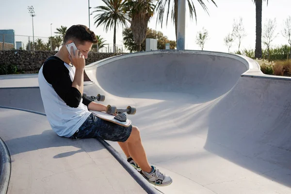 Jonge Man Praten Door Smartphone Tijdens Het Zitten Met Skateboard — Stockfoto