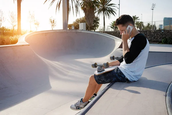 Jonge Man Praten Door Smartphone Tijdens Het Zitten Met Skateboard — Stockfoto