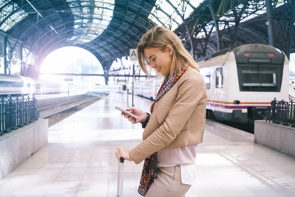 鉄道駅のプラットホームで電車を待っている間にスマート フォンを使用して若い魅力的な女性実業家 — ストック写真