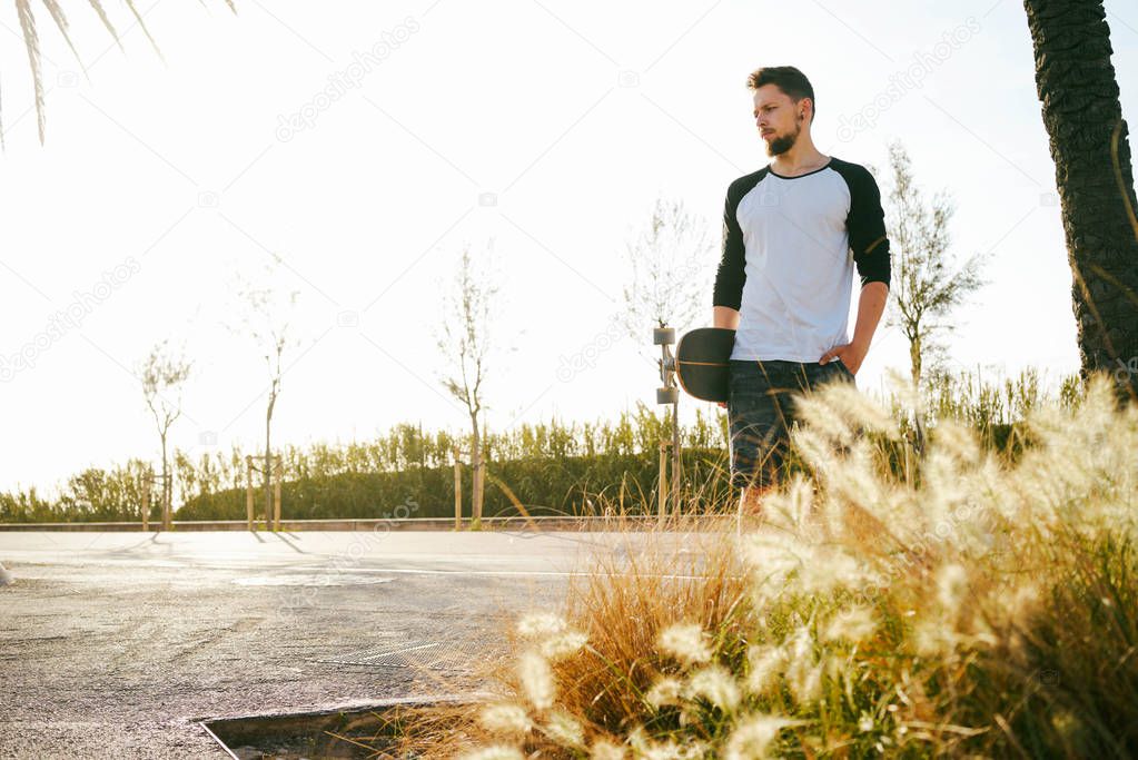 Young man in casual clothes standing in a skate zone with skateboard 