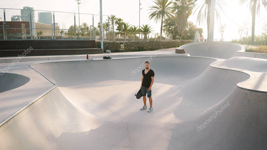 Young man in casual clothes standing in a skate zone with skateboard 