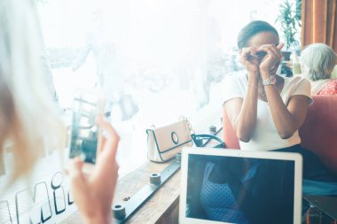 İki kadın arkadaş bir kafede bir cep telefonu kamera fotoğraf çekerken eğleniyor musun