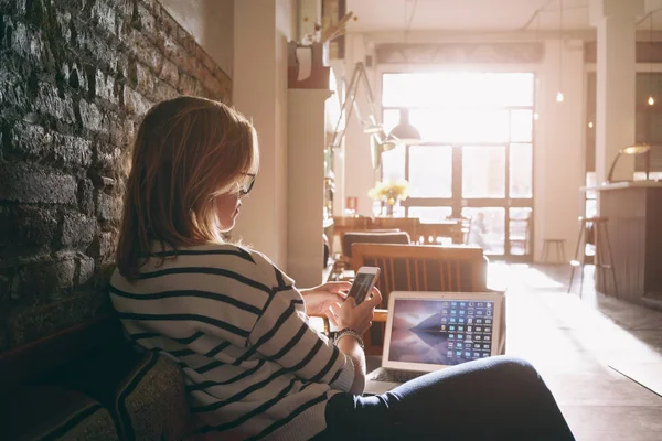 young beautiful businesswoman writes a message on smartphone during the lunch break while sitting at table with laptop