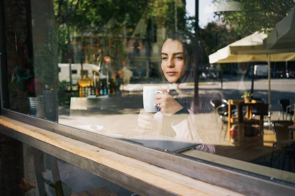 コーヒー ショップのウィンドウの後ろにお茶を飲む若い美人 — ストック写真