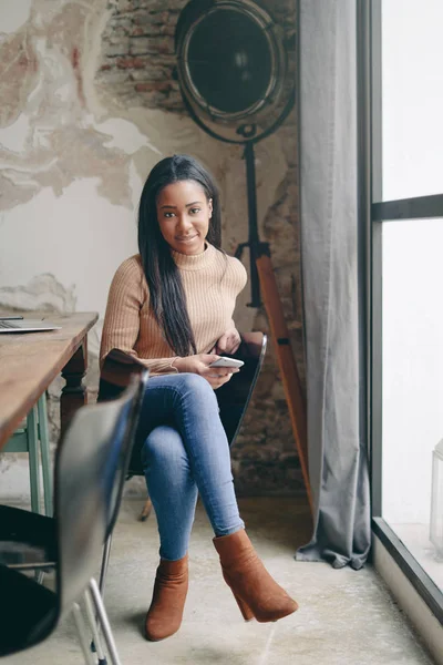 Attractive african american woman with smartphone posing near window