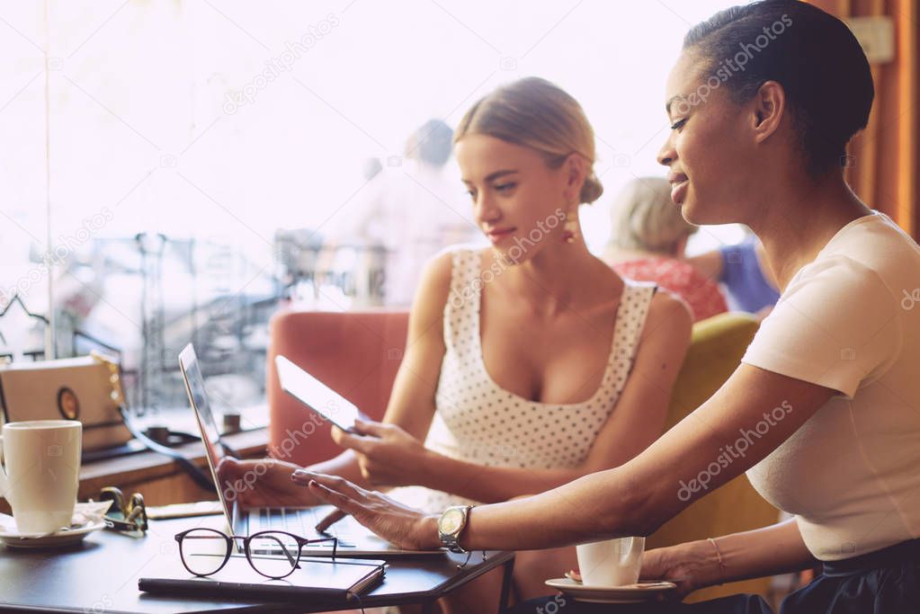 Two businesswomen in casual clothes using digital devices and discussing work cases while having brunch in a cafe