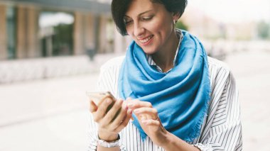 Beyaz gömlek ve eşarp bir sokakta duran smartphone kullanarak Mavi giyen genç çekici kadın