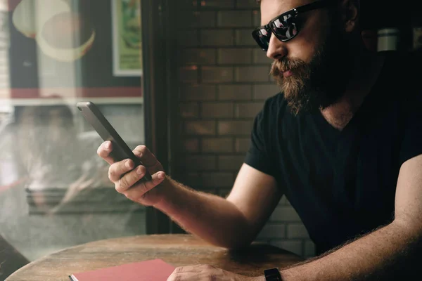 Stilig Skäggig Man Bär Solglasögon Tittar Skärmen Smartphone Coffee Shop — Stockfoto