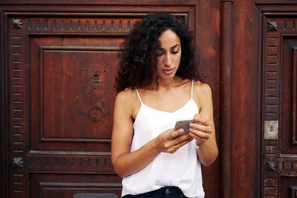 Young Woman Using Smartphone While Standing Wooden Door — Stock Photo, Image