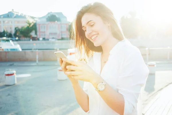 Piękna Młoda Kobieta Trzymając Smartfon Rękach Stojącą Ulicy Słoneczny Dzień — Zdjęcie stockowe