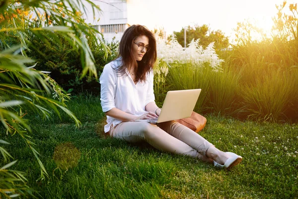 穿着休闲服的漂亮年轻女子正坐在一台笔记本电脑上工作 — 图库照片