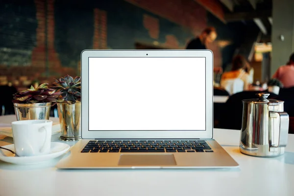 A front view of a modern laptop with white blank screen on the blurred cafe background. A laptop with empty white screen placed with a cup of coffee on a table in a restaurant